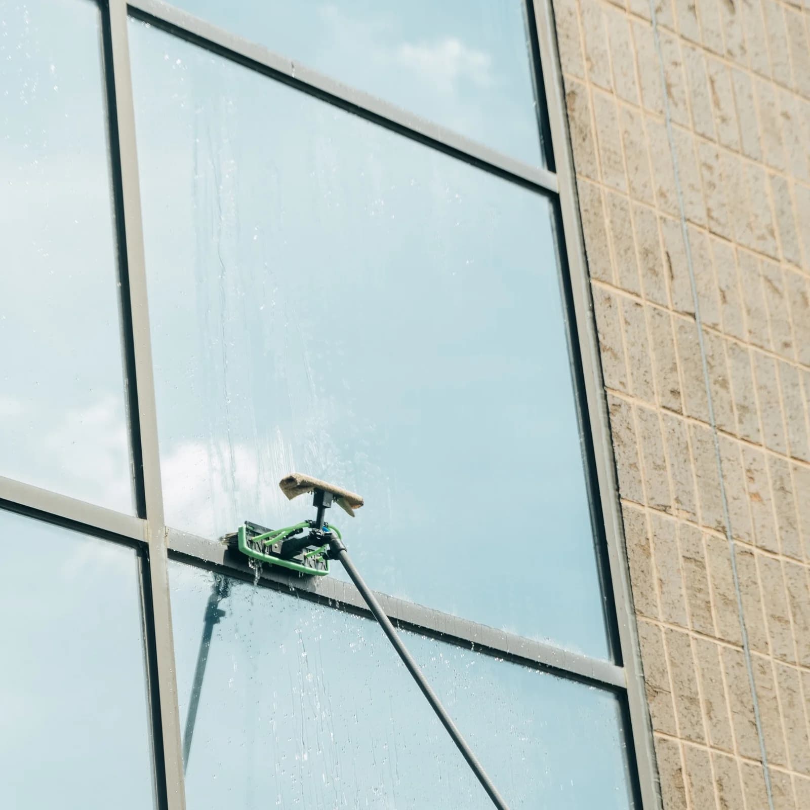 Water-fed brush streaking down a commercial window, reflecting the sky