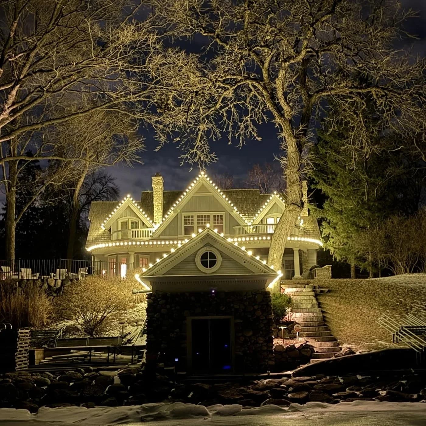 Lakeside home with icicle roofline lighting on every gable, framed by bare winter trees