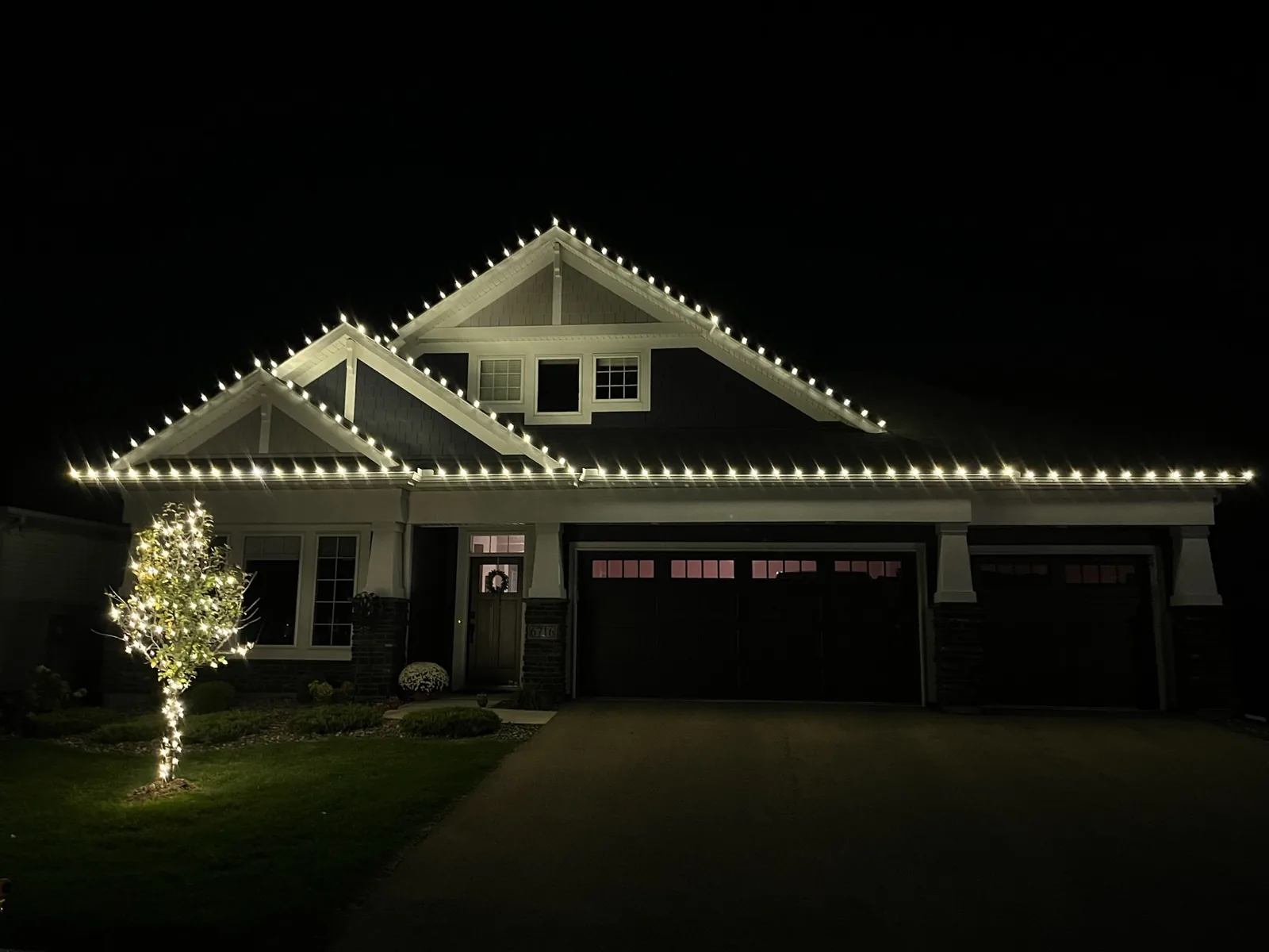 Warm white C9 lit roofline on a craftsman home with mini lights wrapped on the small front-yard tree — holiday lighting Twin Cities MN