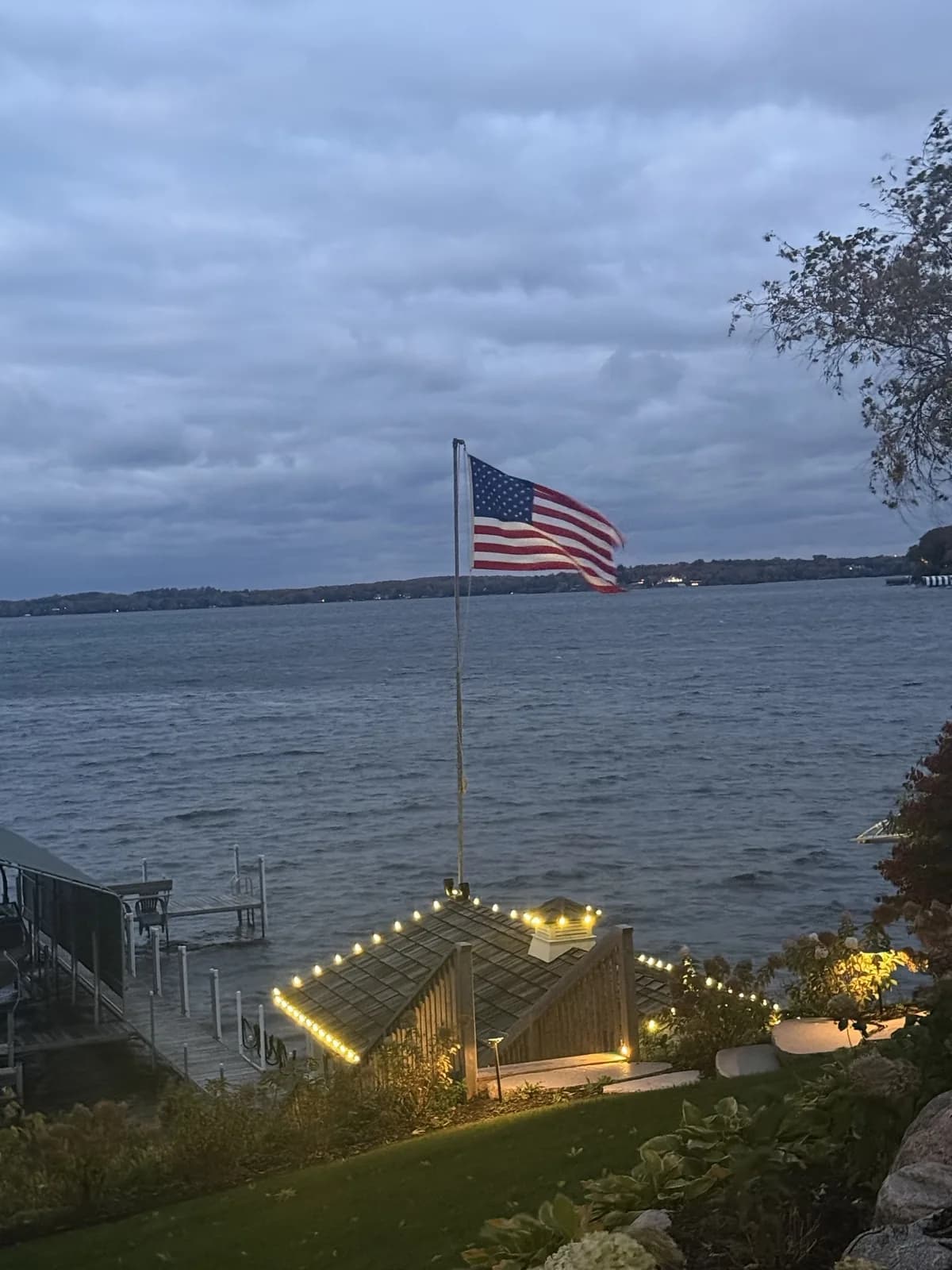 Lake Minnetonka boathouse trimmed in warm white C9 lights with the flag flying over the lake at dusk