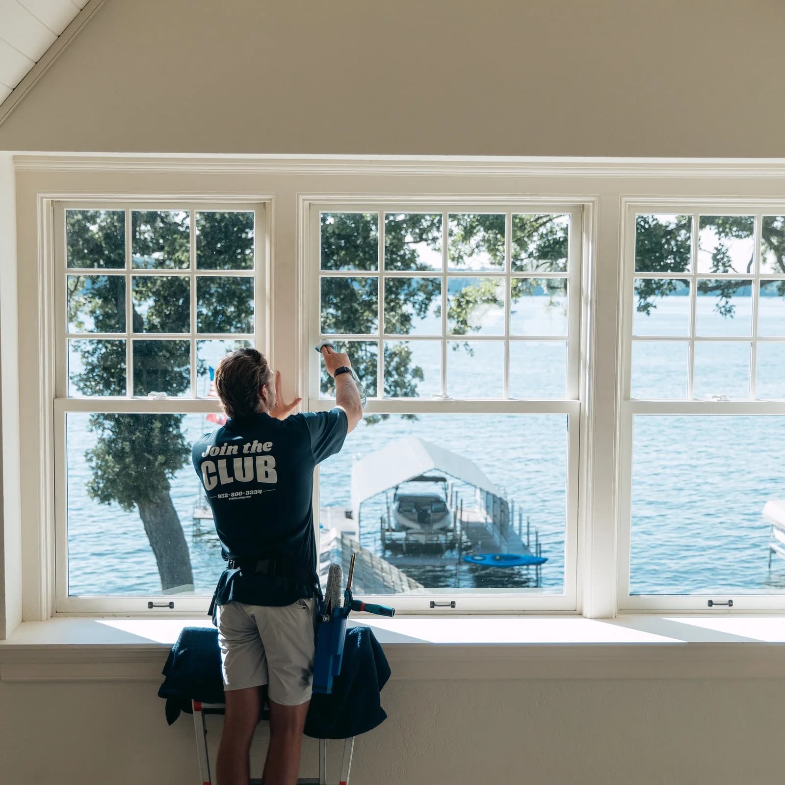 FCR technician on a ladder cleaning tall interior windows at a lake house