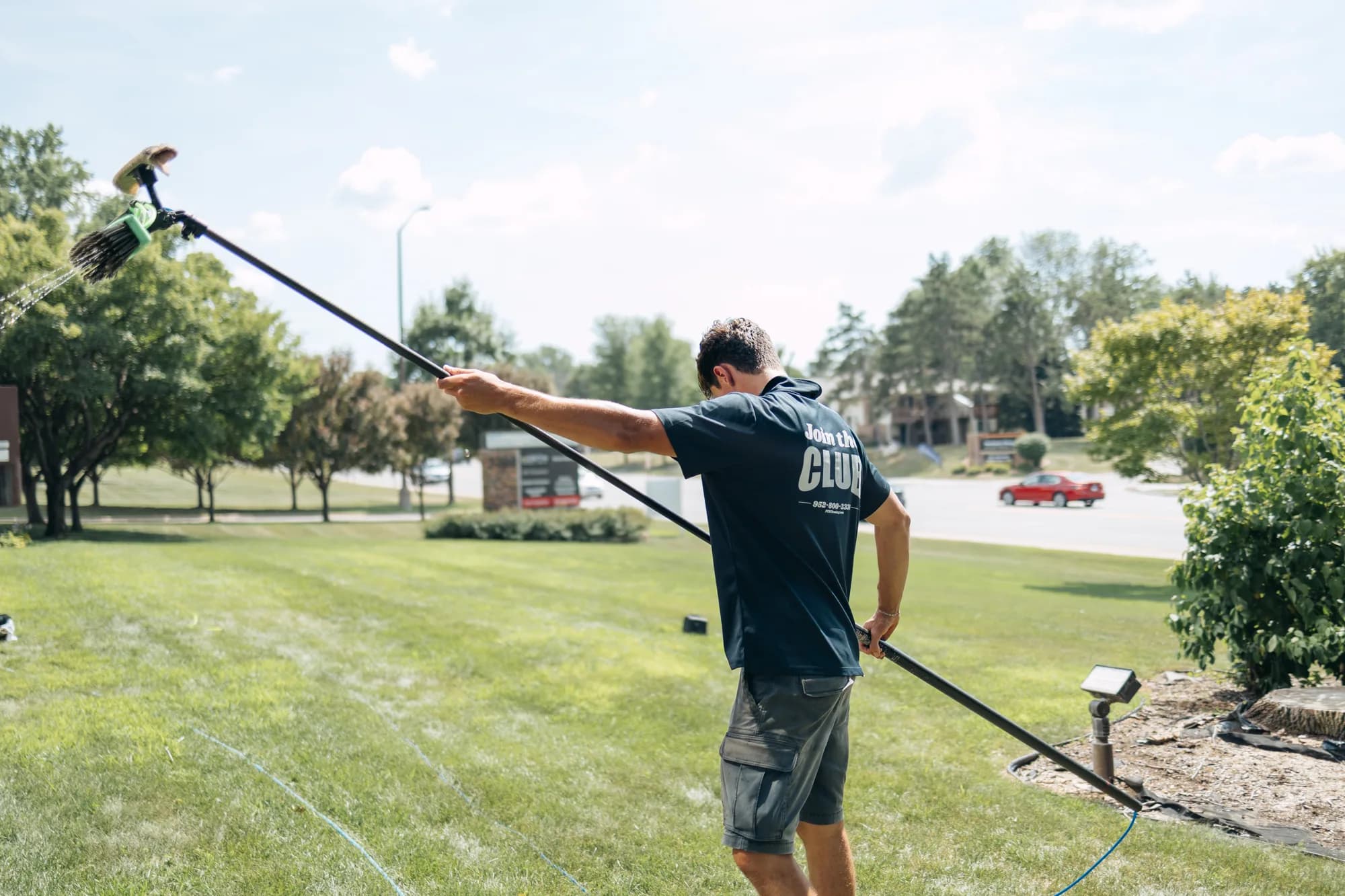 Technician raising the water-fed brush overhead — commercial window cleaning Twin Cities