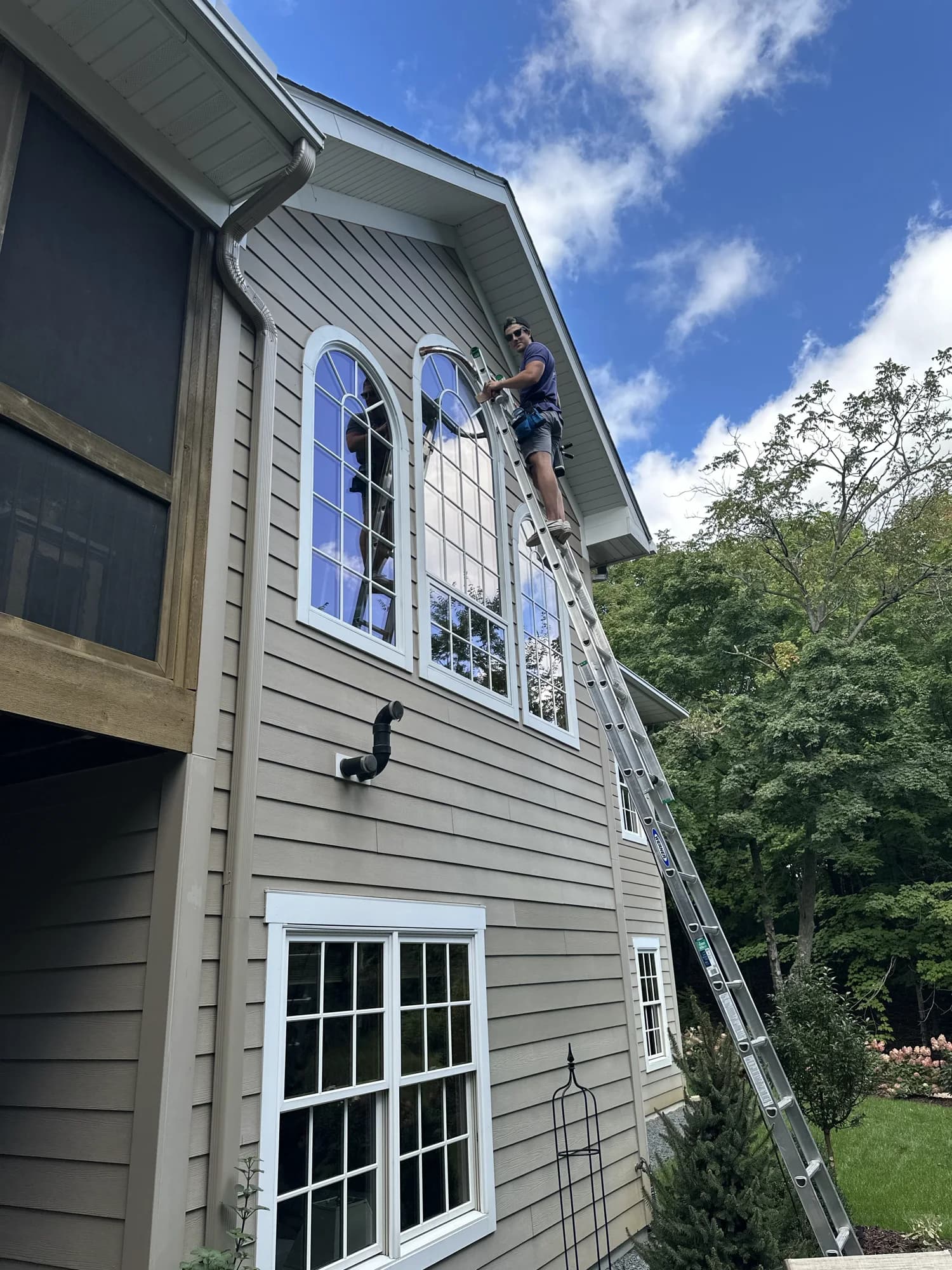 Technician detailing tall arched exterior windows — sky-reflecting clean glass